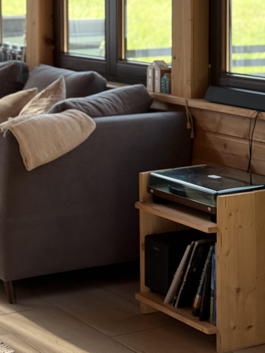 Gramofon na drewnianej szafce, obok płyty i kanapa z lnianym kocem